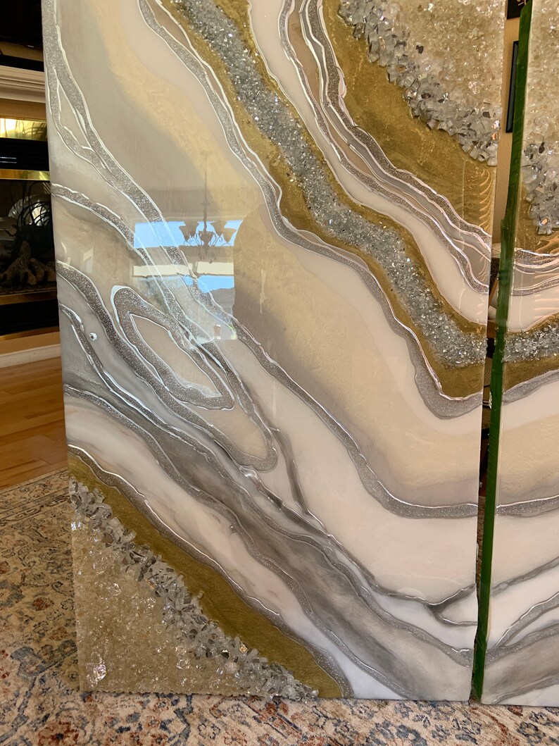 Puede incluir: Dos paneles de arte de resina con un dise&ntilde;o abstracto blanco, dorado y plateado. La resina es transparente y tiene un acabado brillante. El dise&ntilde;o presenta l&iacute;neas en espiral y cristales incrustados.