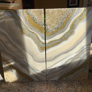 Puede incluir: Dos paneles de arte de resina abstracta blanca, dorada y plateada con un dise&ntilde;o de geoda. Los paneles est&aacute;n separados por una fina grieta.