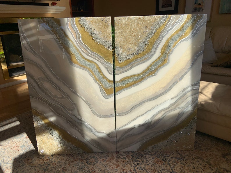 Puede incluir: Dos paneles de arte de resina abstracta blanca, dorada y plateada con un dise&ntilde;o de geoda. Los paneles est&aacute;n separados por una fina grieta.