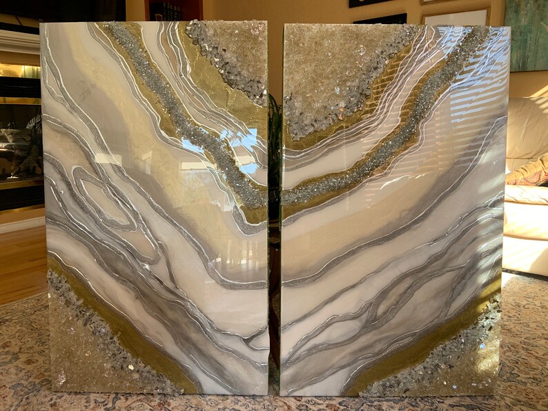 Puede incluir: Dos piezas de arte abstracto con un esquema de color blanco, gris y dorado. Las piezas presentan un dise&ntilde;o de remolino, fluido con brillo y cristales incrustados.
