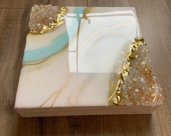 May include: White square canvas with a blue and gold abstract design. The design features gold leaf accents and white crystals.