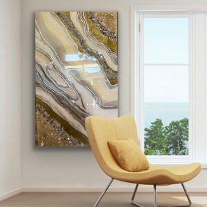 Puede incluir: Una pintura abstracta contempor&aacute;nea con l&iacute;neas de brillo dorado, marr&oacute;n y plateado que se arremolinan sobre un fondo blanco. La pintura est&aacute; colgada en una pared blanca en una habitaci&oacute;n con una silla amarilla y una ventana con vista al mar.