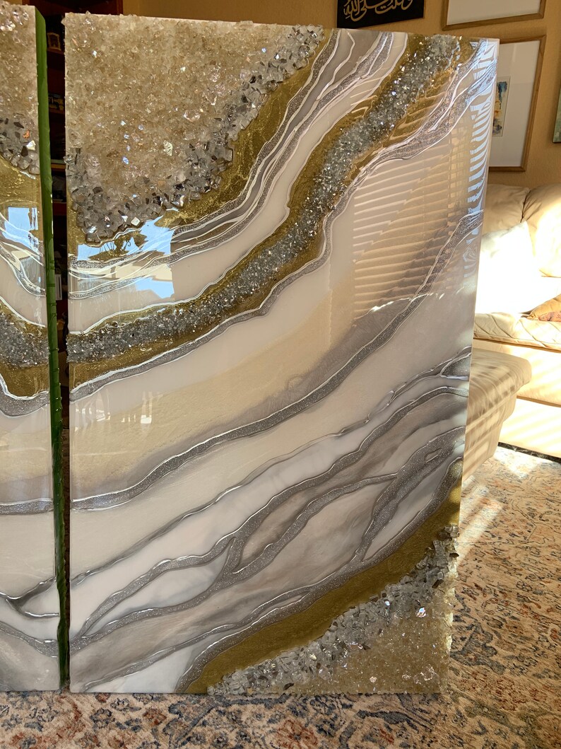 Puede incluir: Dos grandes paneles de arte rectangulares de resina blanca con purpurina dorada y plateada y cristales de cuarzo transparentes incrustados en la resina. Los paneles tienen un patr&oacute;n de remolino, similar al del &aacute;gata.