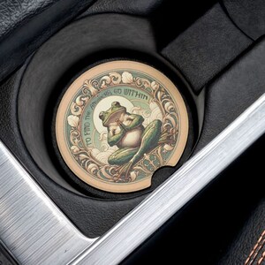 May include: A round, brown coaster with a green frog design. The frog is sitting on a lily pad and has the words "To find peace go within" written around it.