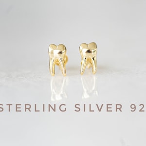 Könnte beinhalten: Ein Paar goldfarbene Ohrringe aus Sterlingsilber 925 in Zahnform.