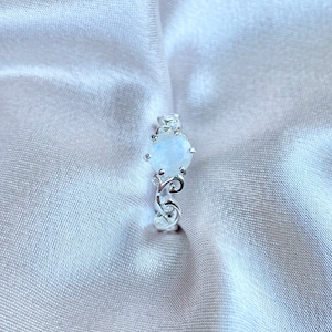 May include: A silver ring featuring a white moonstone set in an intricate, ornate design.