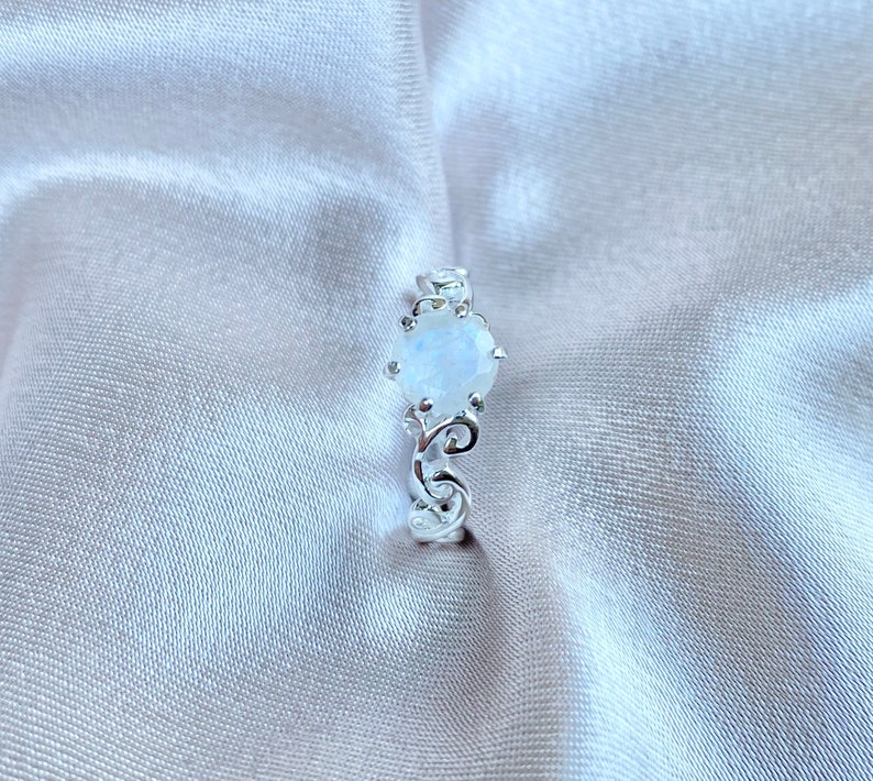 May include: A silver ring featuring a white moonstone set in an intricate, ornate design.