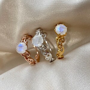 May include: Three rings featuring a moonstone gemstone set in a delicate, ornate, scroll-like design. The rings are in gold, silver, and rose gold.