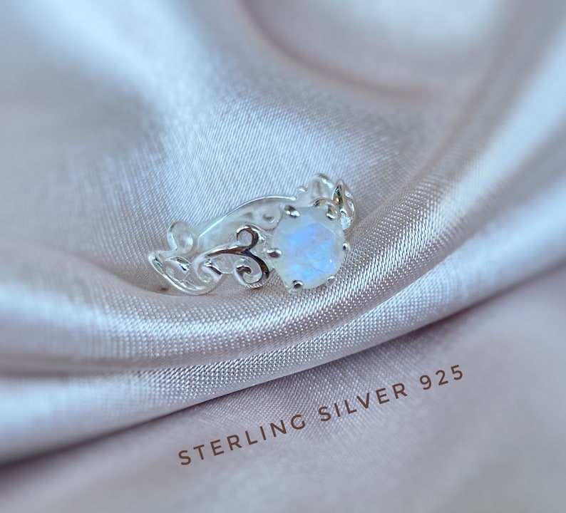 May include: A silver ring with a delicate, ornate design featuring a moonstone gemstone. The ring is marked "STERLING SILVER 925".