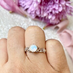 May include: A silver ring featuring a white moonstone set in a delicate floral design.