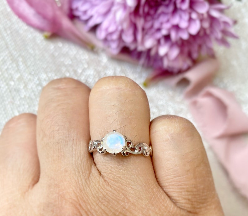 May include: A silver ring featuring a white moonstone set in a delicate floral design.