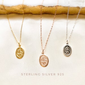 Puede incluir: Tres collares de plata con colgantes ovalados que representan una imagen religiosa de San Cristóbal. Los collares se muestran sobre una superficie blanca con el texto "STERLING SILVER 925".