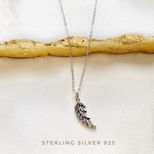 K&ouml;nnte beinhalten: Eine silberne Halskette mit einem einzelnen Fl&uuml;gel-Anh&auml;nger. Der Anh&auml;nger ist mit einem strukturierten Design verziert und die Kette ist in einem zarten, verlinkten Stil gehalten. Der Text "STERLING SILVER 925" ist unterhalb des Anh&auml;ngers sichtbar.