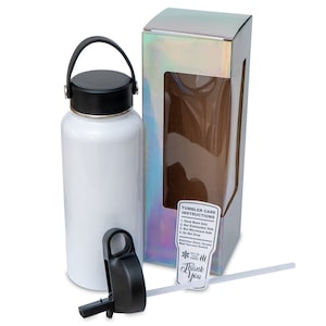 May include: A white stainless steel tumbler with a black lid and handle, next to its iridescent box. The tumbler has a straw and a separate black lid. A sticker on the box reads "Thank You" and "Tumbler Care Instructions."