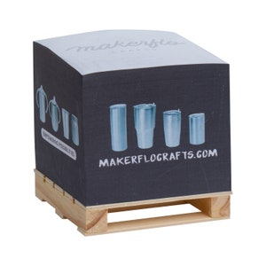 May include: A black and white notepad with a pallet base. The notepad has a white top with the text "makerflo crafts" in gray. The front of the notepad has a black background with a white graphic of five stainless steel tumblers and the text "makerflocrafts.com". The text "empowering possibilities" is also on the notepad.