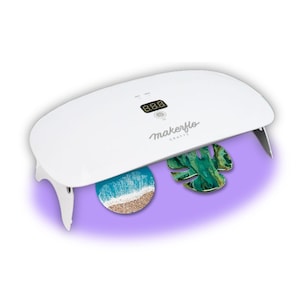 May include: White UV resin curing lamp with a digital timer display. The lamp is turned on and the display reads "8.8.8". The text "makerflo crafts" is printed on the lamp. Two resin art pieces are sitting under the lamp, one is a beach scene and the other is a green leaf.