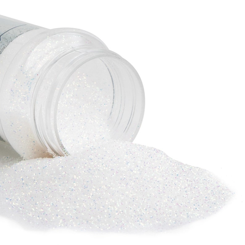 May include: A clear plastic container tipped over, spilling iridescent white glitter onto a white surface. The glitter sparkles with hints of blue and silver, creating a shimmering effect. The container is partially visible, showing its open top.