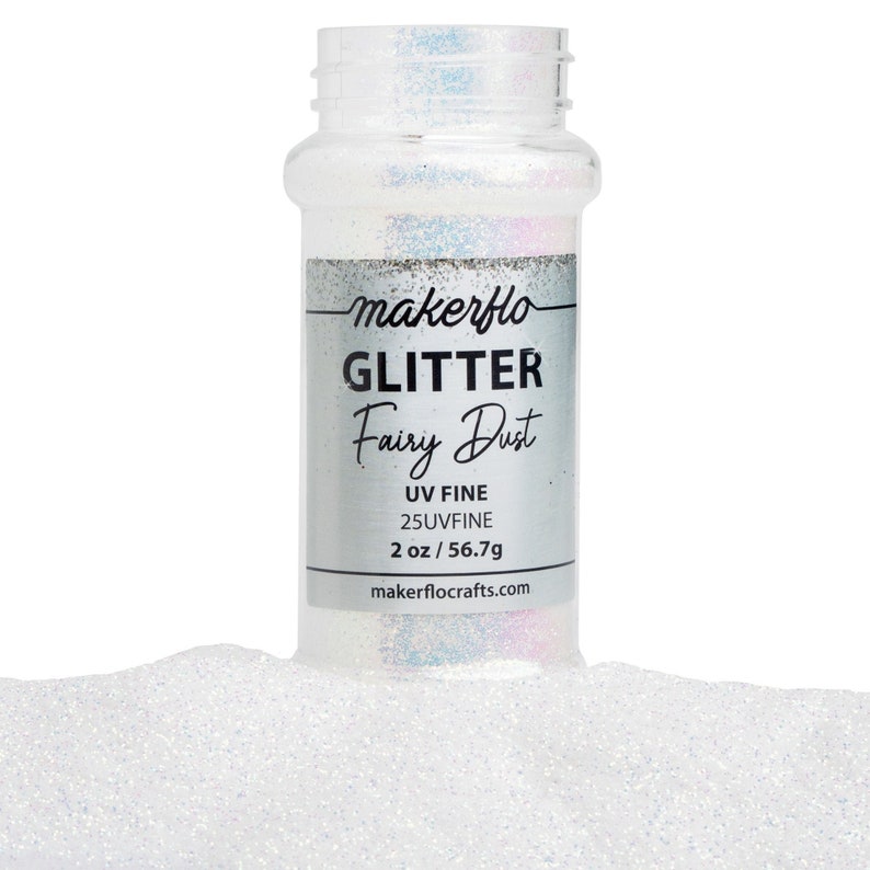 May include: A clear plastic bottle of "Fairy Dust" glitter, with a silver label. The label reads "makerflo GLITTER Fairy Dust UV FINE 2 oz / 56.7g". The glitter is white and iridescent, with a fine texture. The bottle is partially surrounded by a pile of glitter.