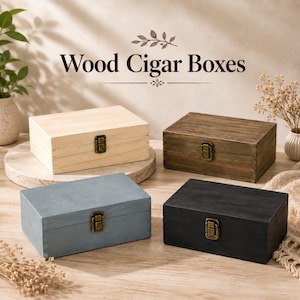 May include: Four rectangular wooden cigar boxes with hinged lids and antique brass-colored metal latches. The boxes are finished in natural light wood, medium brown, slate blue, and black. The text Wood Cigar Boxes is centered above them.