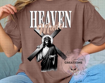 May include: Brown t-shirt with the text "HEAVEN Made" in white and tan. The shirt features a graphic of Jesus carrying a cross. The image is a religious design.
