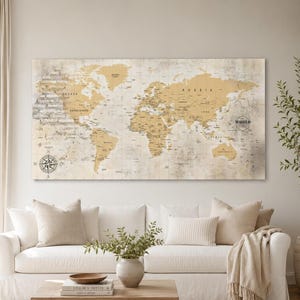 Può includere: Una grande mappa del mondo rettangolare, nei toni del beige e dell'oro, è appesa sopra un divano bianco. La mappa presenta i contorni dei paesi e una rosa dei venti. La parola "WORLD" è stampata sulla mappa. La stanza è decorata in toni neutri.