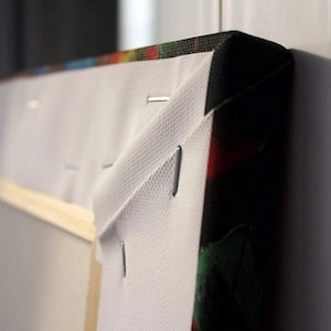 May include: Close-up of the edge of a canvas print, showing the white canvas wrapped around the wooden frame and secured with staples. The print features a colorful abstract design.