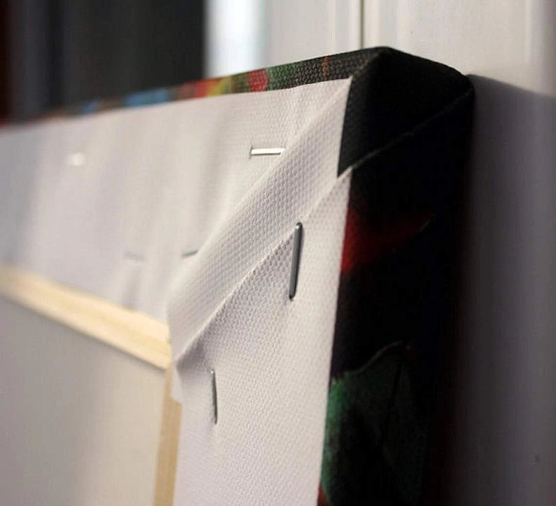 May include: Close-up of the edge of a canvas print, showing the white canvas wrapped around the wooden frame and secured with staples. The print features a colorful abstract design.