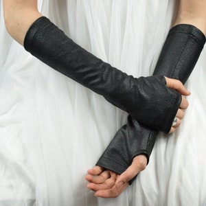 Peut inclure: Une paire de gants noirs sans doigts arrivant au coude, dotés d'une surface texturée et granuleuse. Ces longs chauffe-bras s'étendent des articulations jusqu'au haut de l'avant-bras, avec une coupe ajustée et des coutures latérales visibles.
