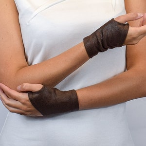 Puede incluir: Guantes sin dedos marrones hechos de un material texturizado. Los guantes cubren la muñeca y parte de la mano, con una abertura para los dedos. Los guantes son de color marrón oscuro y parecen estar hechos de cuero o un material similar.