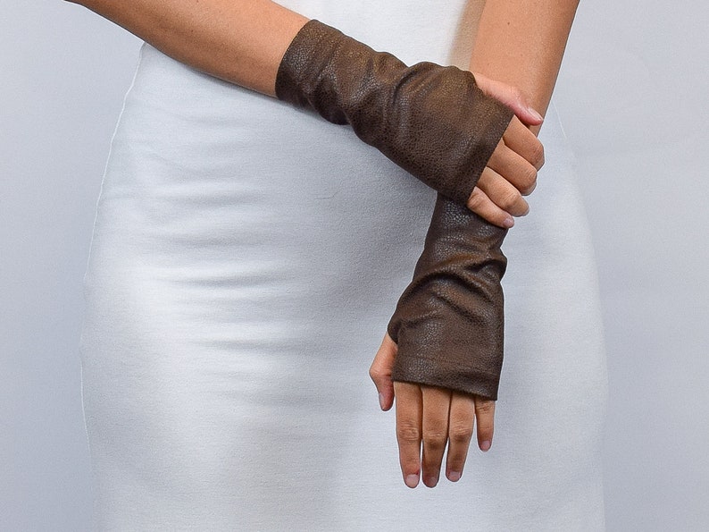 May include: A pair of dark brown fingerless gloves with a textured, pebbled surface. These arm warmers extend from the knuckles to the mid-forearm, featuring a snug fit and a simple opening for the thumb, providing coverage for the hands and wrists.