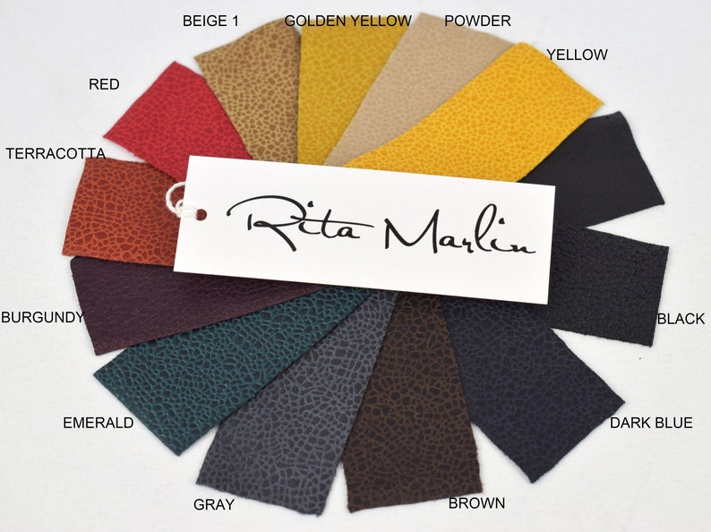 May include: A color swatch sample set featuring twelve textured leather-like material strips arranged in a fan shape. The colors include red, beige, golden yellow, powder, yellow, black, dark blue, brown, gray, emerald, and burgundy. A white tag with the text Rita Marlin is attached.
