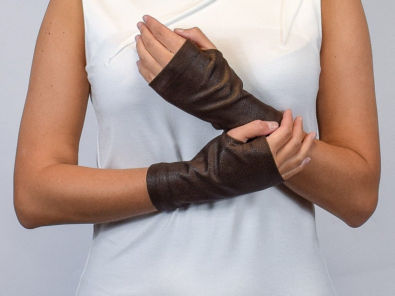 May include: A pair of dark brown fingerless gloves with a textured, slightly metallic finish. The gloves extend from the knuckles to the mid-forearm, featuring a simple, fitted design that leaves the fingers and thumbs exposed for full dexterity.