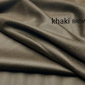 May include: A piece of fabric in a khaki brown color with a textured, slightly distressed surface appearance. The material is draped in soft folds, creating shadows and highlights across the surface. The text khaki BROWN is printed on the fabric.
