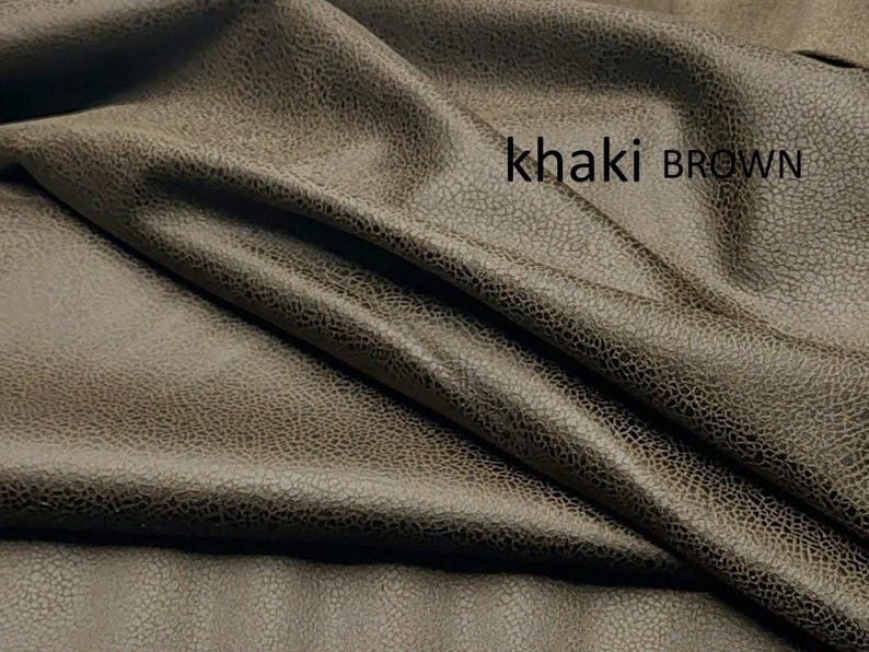 May include: A piece of fabric in a khaki brown color with a textured, slightly distressed surface appearance. The material is draped in soft folds, creating shadows and highlights across the surface. The text khaki BROWN is printed on the fabric.