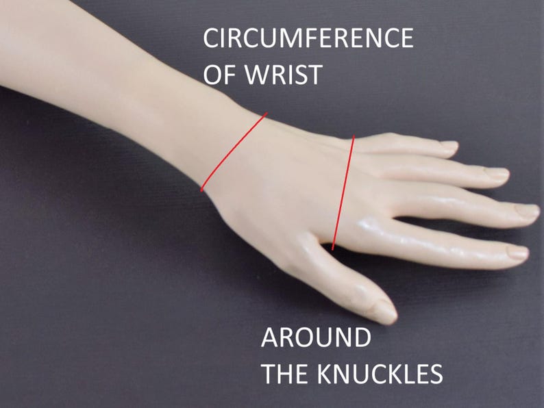 May include: A beige mannequin hand and forearm showing measurement lines. Text reads CIRCUMFERENCE OF WRIST above a red line around the wrist, and AROUND THE KNUCKLES below a red line across the hand, indicating where to measure for jewelry sizing.