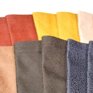 May include: A collection of rectangular fabric swatches arranged in a fan pattern. The colors include shades of red, yellow, cream, tan, dark brown, and a dark blue with a textured, crackled pattern visible on the surface of each piece.