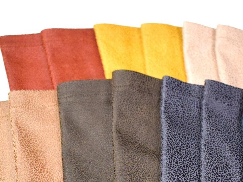 May include: A collection of rectangular fabric swatches arranged in a fan pattern. The colors include shades of red, yellow, cream, tan, dark brown, and a dark blue with a textured, crackled pattern visible on the surface of each piece.