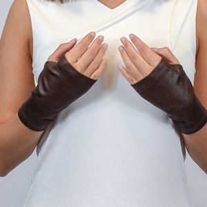 May include: A pair of dark brown fingerless gloves with a textured surface. The gloves cover the hands from the knuckles down to the wrists, leaving the fingers and thumbs exposed. The material appears to have a matte finish and a subtle grain.
