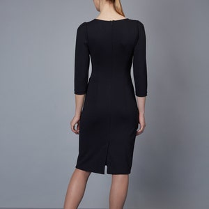 May include: A black knee-length dress with three-quarter length sleeves, a round neckline, and a vertical zipper closure along the center back. The garment features a straight silhouette with a small slit at the bottom hem of the back panel.