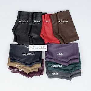 May include: A collection of fingerless gloves in various colors including black, red, brown, dark blue, lilac, beige, burgundy, emerald, and grey. Each pair features a textured finish and a thumb opening. A white tag with the text Rita Marlin is visible.