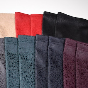 May include: A collection of rectangular fabric pouches featuring a textured, crackled surface pattern. The pouches are arranged in a fan-like display and come in various colors including beige, red, black, dark gray, teal, navy, and deep purple.