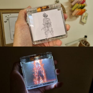 May include: A clear, handheld device with a screen displaying a drawing of a muscular character. The device is lit up, showing the character in a fiery, orange glow. The device is held in a hand.
