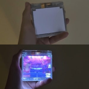 May include: A clear plastic Game Boy Advance SP with a bright pink and blue light emanating from the screen. The screen displays a video game with a blue and white background.