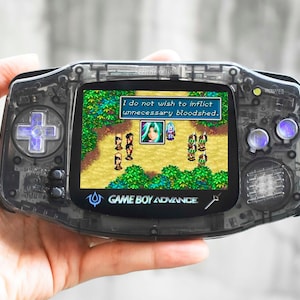 May include: A black Game Boy Advance handheld gaming console with a transparent shell. The screen displays a video game with a text box that reads "I do not wish to inflict unnecessary bloodshed."