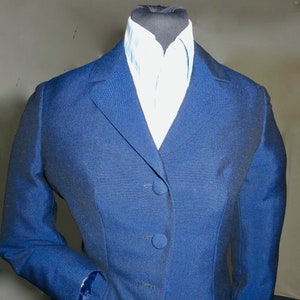 Könnte beinhalten: Ein dunkelblauer Blazer mit einreihigem Verschluss und drei Knöpfen. Der Blazer hat einen Schalkragen und eine Tasche auf der linken Seite. Der Blazer wird über einem weiß-blau karierten Hemd getragen.