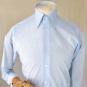 Op de afbeelding: Lichtblauw overhemd met lange mouwen, een klassieke kraag en een knoopsluiting. Het overhemd heeft een subtiel patroon en wordt op een mannequin gepresentereerd. De manchetten hebben goudkleurige manchetknopen.