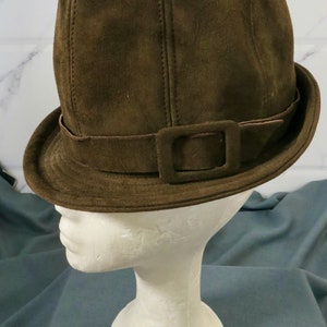 May include: A brown suede fedora hat with a wide brim and a buckle on the band.