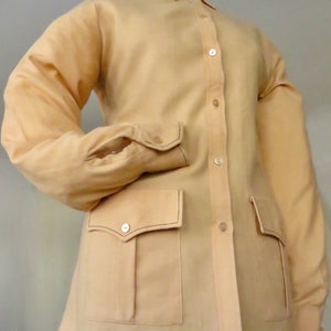 May include: A light beige long-sleeved shirt with a button-up front and two large patch pockets. The shirt has a collar and a slightly relaxed fit.