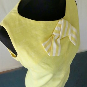 May include: A sleeveless yellow dress with a white and yellow striped bow at the neckline.