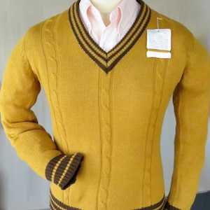 Puede incluir: Un suéter de punto de cable amarillo mostaza con rayas marrones y amarillas en el cuello, los puños y el dobladillo.